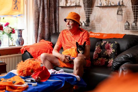 Man in oranje outfit kijkt voetbal in zijn huis